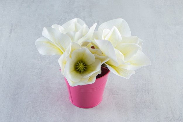 Witte bloemen in een roze emmer, op de witte tafel.