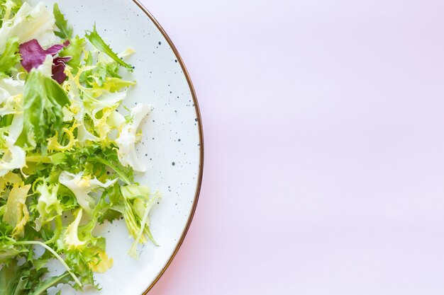 Witte ceramische plaat met verse salade op lichtroze oppervlakte