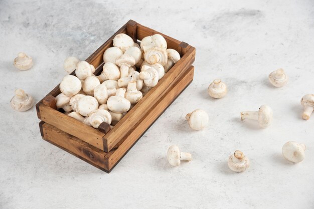 Witte champignons in een houten dienblad op een marmeren tafel.