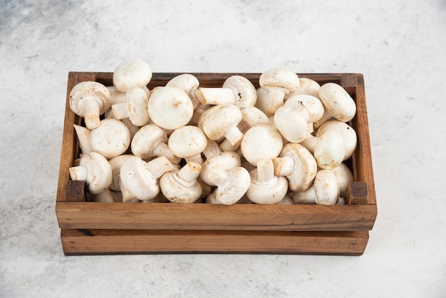 Witte champignons in een houten dienblad op een marmeren tafel.