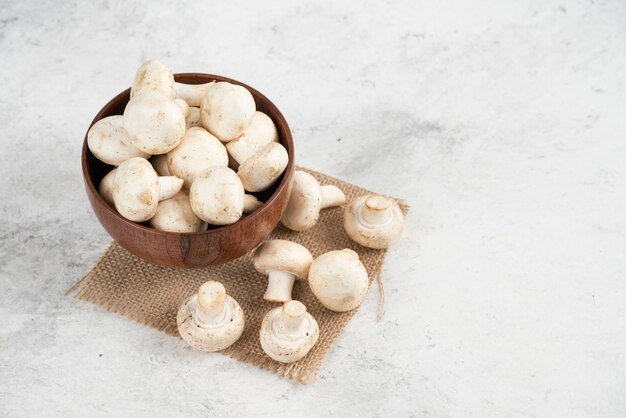 Witte champignons in een houten kopje op een stuk jute.