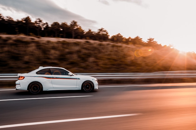 Witte coupé sedan rijden op de weg in de zonsondergang