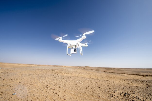 Witte drone vliegt over een uitgedroogd woestijngebied tegen een blauwe lucht