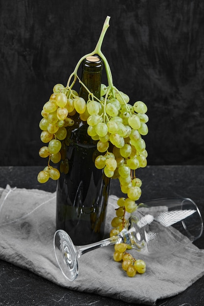 Witte druiven rond een fles wijn en een leeg glas op donkere ondergrond met grijs tafelkleed