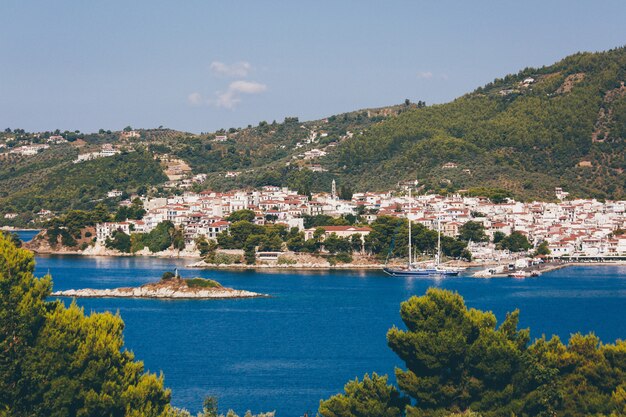 Witte en bruine huizen dichtbij blauwe oceaan die door bergen met bomen in Skiathos, Griekenland wordt omringd