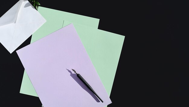 Witte envelop en veelkleurig briefpapier op donkere achtergrond, bovenaanzicht met kopieerruimte. Minimalistische mockup met envelop en lege kaart voor vakantiegroeten, plat gelegd