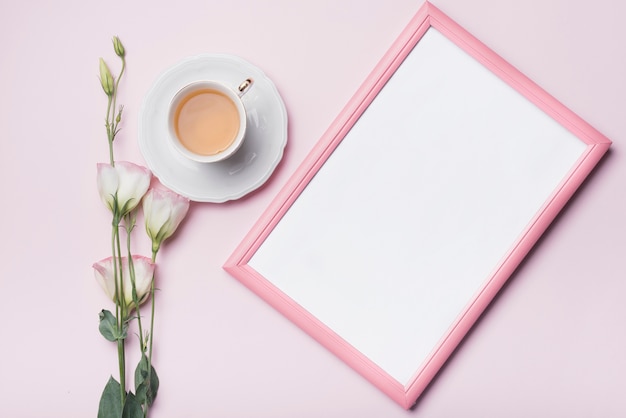 Gratis foto witte fotolijst; kopje thee en eustoma bloemen tegen roze achtergrond