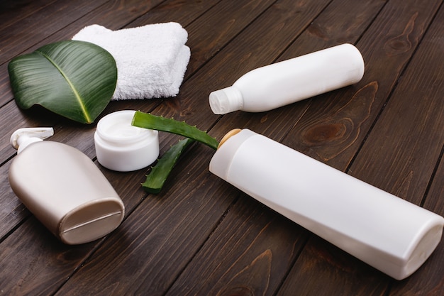 Witte handdoek, flessen shampoo en conditioner liggen op een tafel met groen blad en aloë
