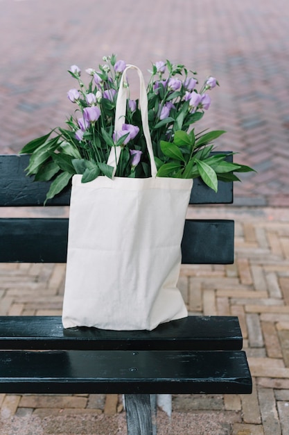 Witte katoenen handtas met prachtige paarse eustoma bloemen in de zwarte bank