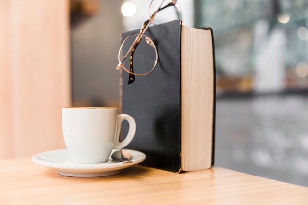 Witte koffiekop met oogglazen en boek op houten lijst