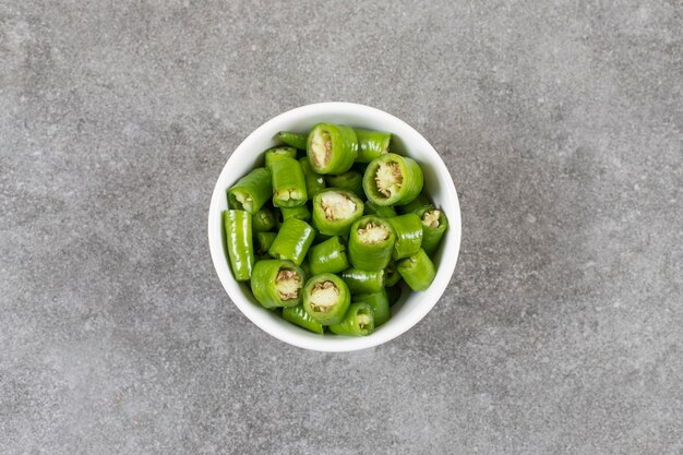 Witte kom met gesneden chilipepers op stenen oppervlak.