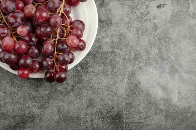 Witte plaat en rode heerlijke druiven op marmeren tafel.