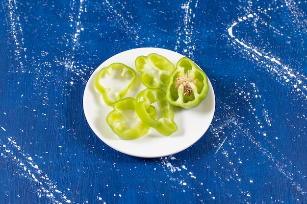 Witte plaat met groene paprikaringen op marmeren oppervlak
