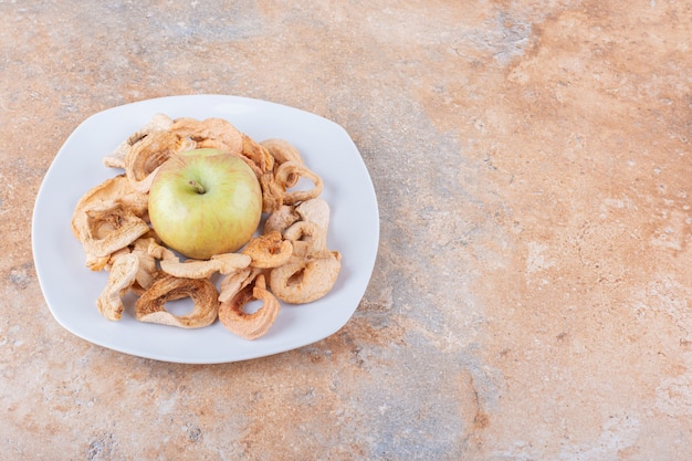 Witte plaat van droge appelringen en verse groene appel op marmeren tafel. Hoge kwaliteit foto