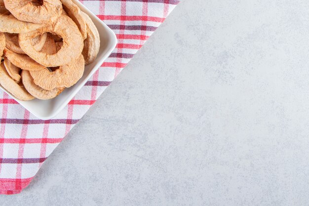 Witte plaat van gezonde gedroogde appelringen op stenen achtergrond.