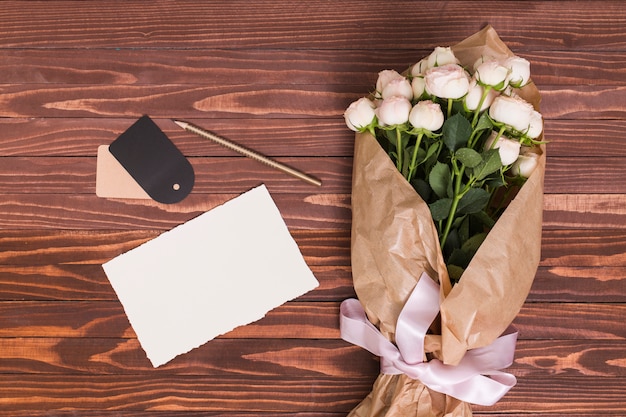 Witte rozen boeket; wit papier; potlood en prijskaartje tegen houten achtergrond