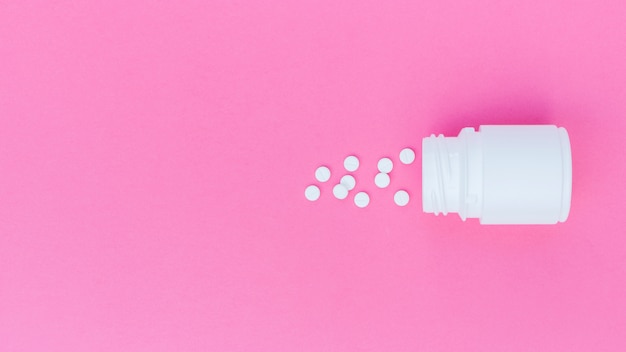 Witte tabletten gemorst uit de plastic fles op roze achtergrond