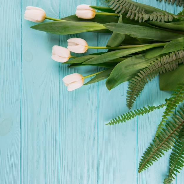 Gratis foto witte tulpenbloemen met varenbladeren op houten lijst