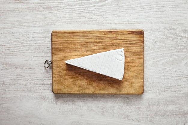 Witte verse driehoek van smakelijke brie kaas op snijplank geïsoleerd op een witte leeftijd houten tafel in het midden. Klaar voor de maaltijd, ontbijt of serveren. Presentatie concept