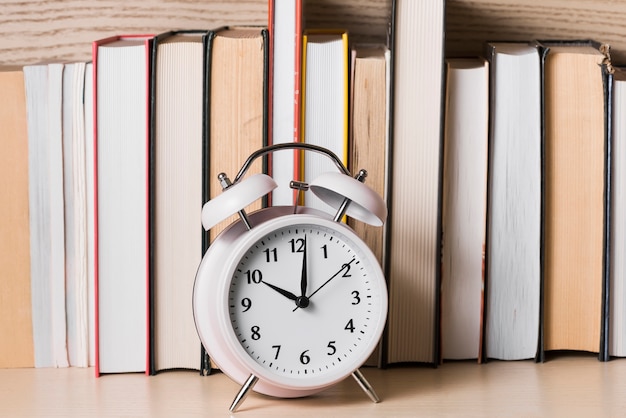 Witte wekker die klok van 10 uur voor boekenrek op houten bureau toont