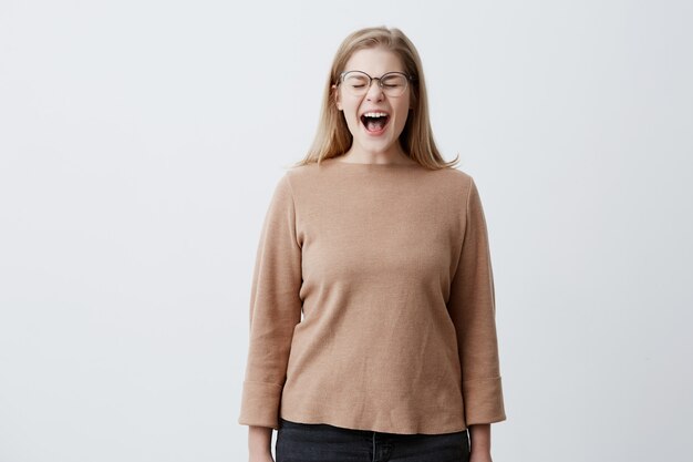 Woedend geïrriteerde jonge vrouw schreeuwt wanhopig, fronst haar gezicht, wordt ergens door gestoord, maakt ruzie met iemand, heeft vertrouwen in haar juistheid. Boos blonde vrouw in glazen schreeuwt