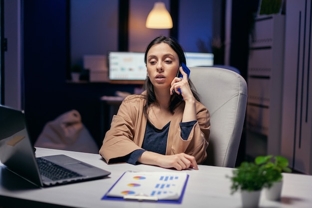 Workaholic-manager die 's avonds telefonisch met de klant praat. Vrouwelijke ondernemer die 's avonds laat in het bedrijfsleven werkt en overuren maakt tijdens een telefoongesprek.