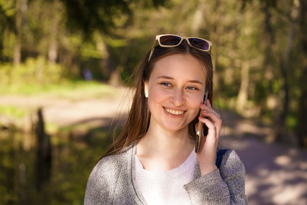 Y een jong mooi meisje met zonnebril loopt en praat aan de telefoon op een zonnige lentedag