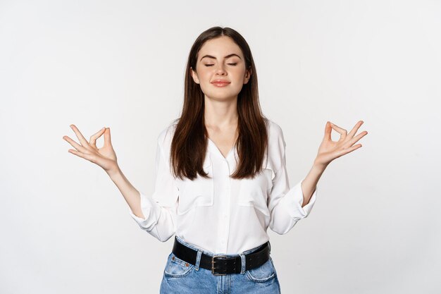 Yoga en mindfulness. Jonge vrouw mediteert met gesloten ogen, ademt vrij en toont mudra nirvana teken, vreedzaam staande op een witte achtergrond.