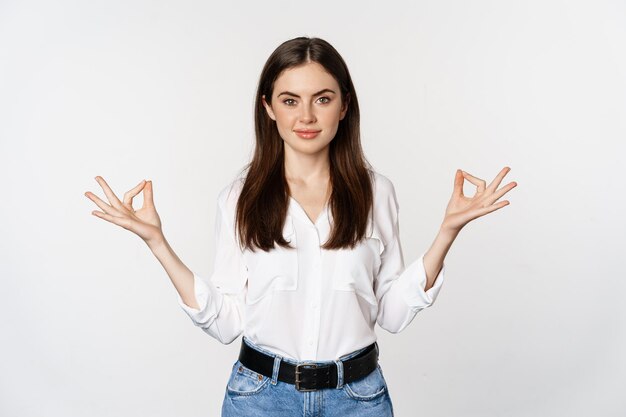 Yoga en mindfulness. Jonge vrouw mediteert met gesloten ogen, ademt vrij en toont mudra nirvana teken, vreedzaam staande op witte achtergrond