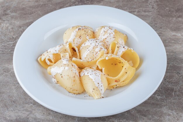Yoghurt op pittige pasta op de plaat, op het marmeren oppervlak.