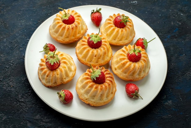 Yummy koekjes van een hoogste mening met rode aardbeien binnen witte plaat op het donkere koekje als achtergrond