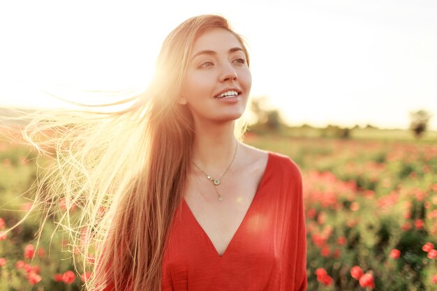 Zachte blonde langharige vrouw met perfecte glimlach poseren op papaverveld in warme zomer zonsondergang.