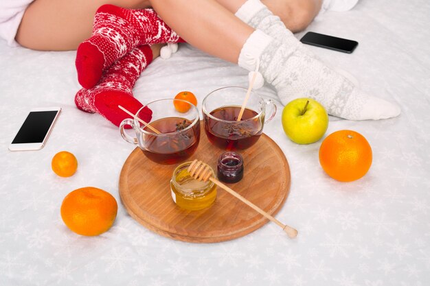 Zachte foto van vrouw en man op het bed met telefoon en fruit. Vrouwelijke en mannelijke benen van paar in warme wollen sokken. Kerstmis, liefde, levensstijlconcept