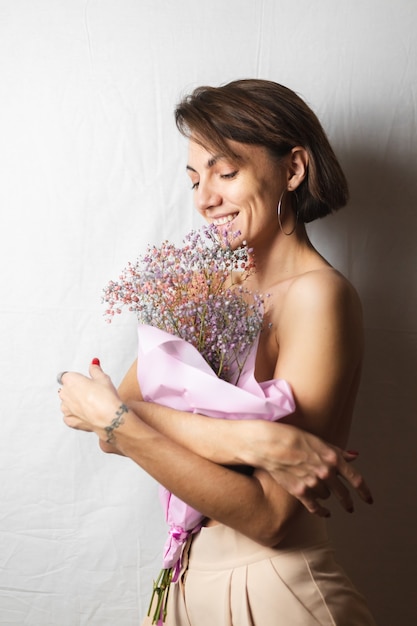 Zachte portret van een jonge vrouw op een witte lap topless met een boeket van droge veelkleurige bloemen en glimlachend schattig, anticipatie van de lente