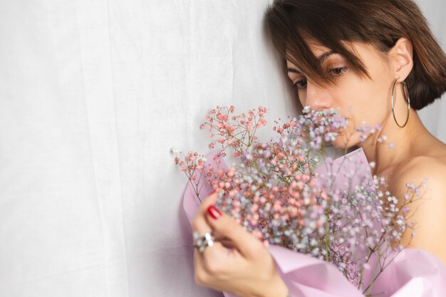 Zachte portret van een jonge vrouw op een witte lap topless met een boeket van droge veelkleurige bloemen en glimlachend schattig, anticipatie van de lente