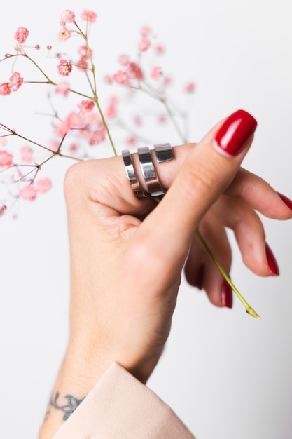 Zachte zachte foto van vrouwenhand met grote ring rode manicure houdt schattige kleine roze gedroogde bloemen op wit.