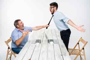 Gratis foto zakelijk conflict. de twee mannen uiten negativiteit terwijl een man de stropdas van haar tegenstander vastgrijpt