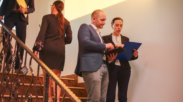 Zakelijk team dat op trappen loopt en collega's ontmoet die werken met een tablet, vrouw in gesprek met corporate executive manager op de trap van het bedrijfsgebouw. Ondernemer overwerken in kantoor trappen.