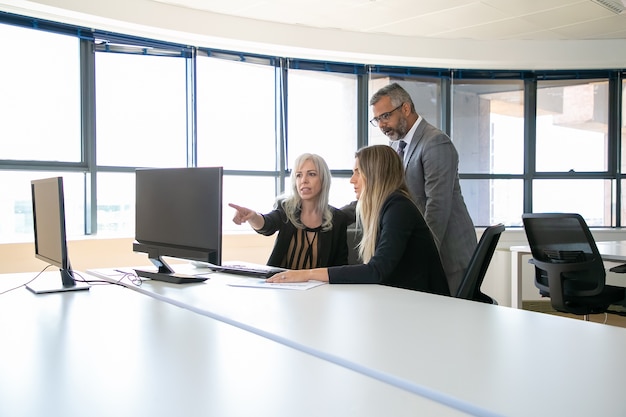 Zakelijke professionals kijken samen naar presentatie op computermonitor, project bespreken, zitten op de werkplek en wijzen op display. Zakelijke communicatie of teamwerk concept