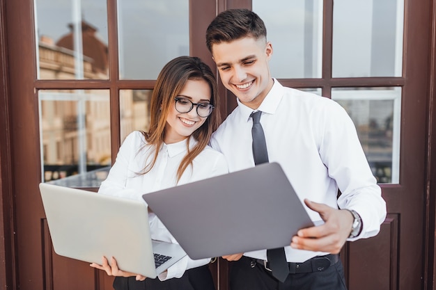 Zakelijke stijl. Jonge mooie vrouw met een bril en een man in een zakelijke afbeelding met een laptop in hun handen glimlachend