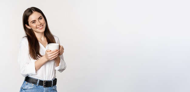 Zakelijke vrouw staat met koffie thee mok en glimlachend drinken uit beker staan blij tegen wh