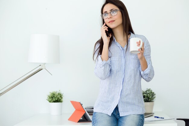 Zaken jonge vrouw met behulp van haar mobiele telefoon in het kantoor.