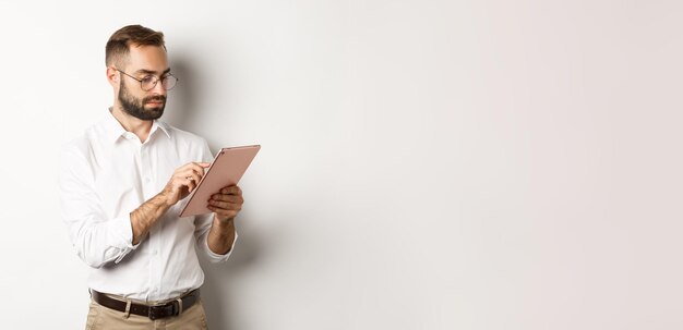 Zakenman die aan digitale tablet werkt en er druk uitziet terwijl hij op een witte achtergrond staat