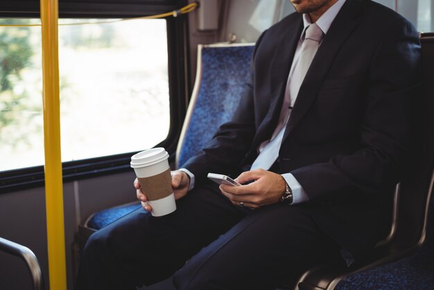 Zakenman die een beschikbare koffiekop houdt en mobiele telefoon met behulp van