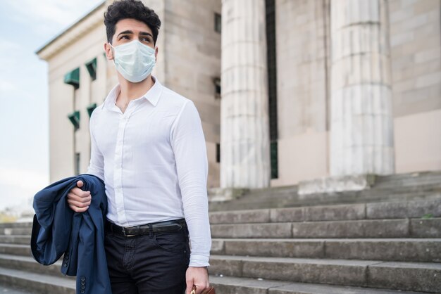 Zakenman die een gezichtsmasker draagt en een aktetas vasthoudt tijdens het wandelen naar het werk buitenshuis.