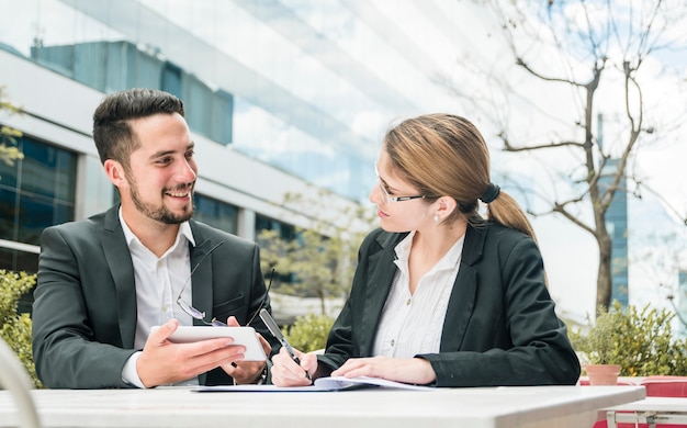 Gratis foto zakenman die mobiele in hand houdt bekijkend haar collega die op het document schrijft