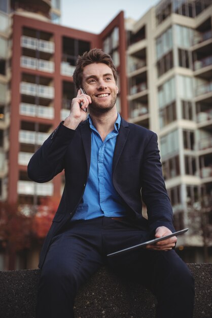 Zakenman die op mobiele telefoon spreekt en digitale tablet houdt