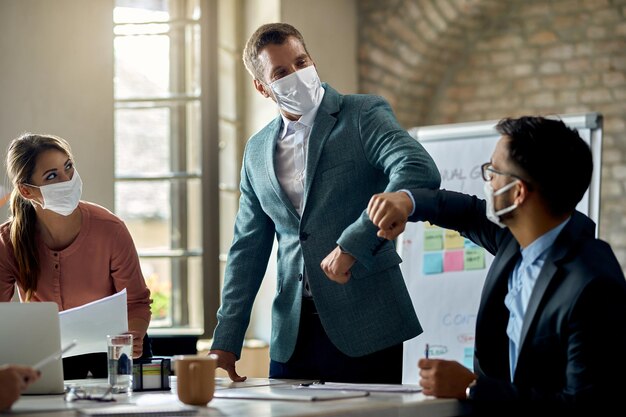 Zakenman en zijn collega die beschermende gezichtsmaskers dragen en ellebogen stoten tijdens het begroeten op kantoor