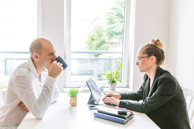 Zakenman het drinken koffie die zijn partner bekijken die aan laptop werken