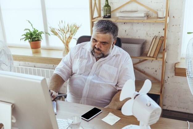 Zakenman in bureau met computer en ventilator die afkoelen, heet, gespoeld voelen